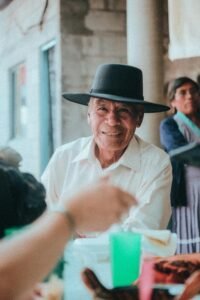 Elderly man smiling while dining outdoors in Puebla, showcasing traditional Mexican culture and attire.