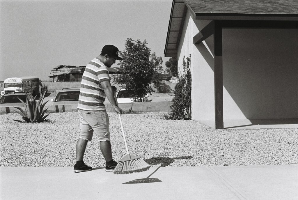 A man sweeping an outdoor pavement next to a house in Tecate, B.C., Mexico.