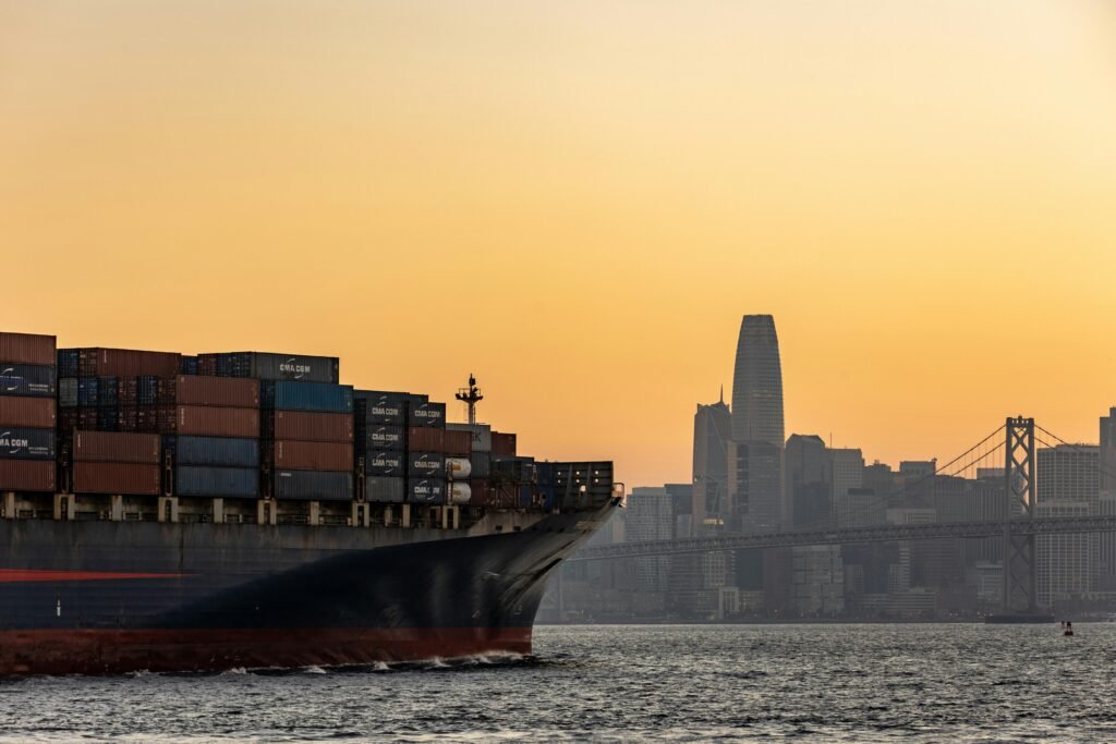 Cargo ship crossing near San Francisco skyline at sunset with iconic cityscape view.